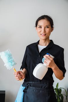 A female housekeeper smiling while holding cleaning tools indoor.