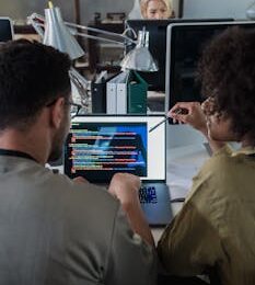 Two developers engage in software programming on a laptop in a modern office setting.